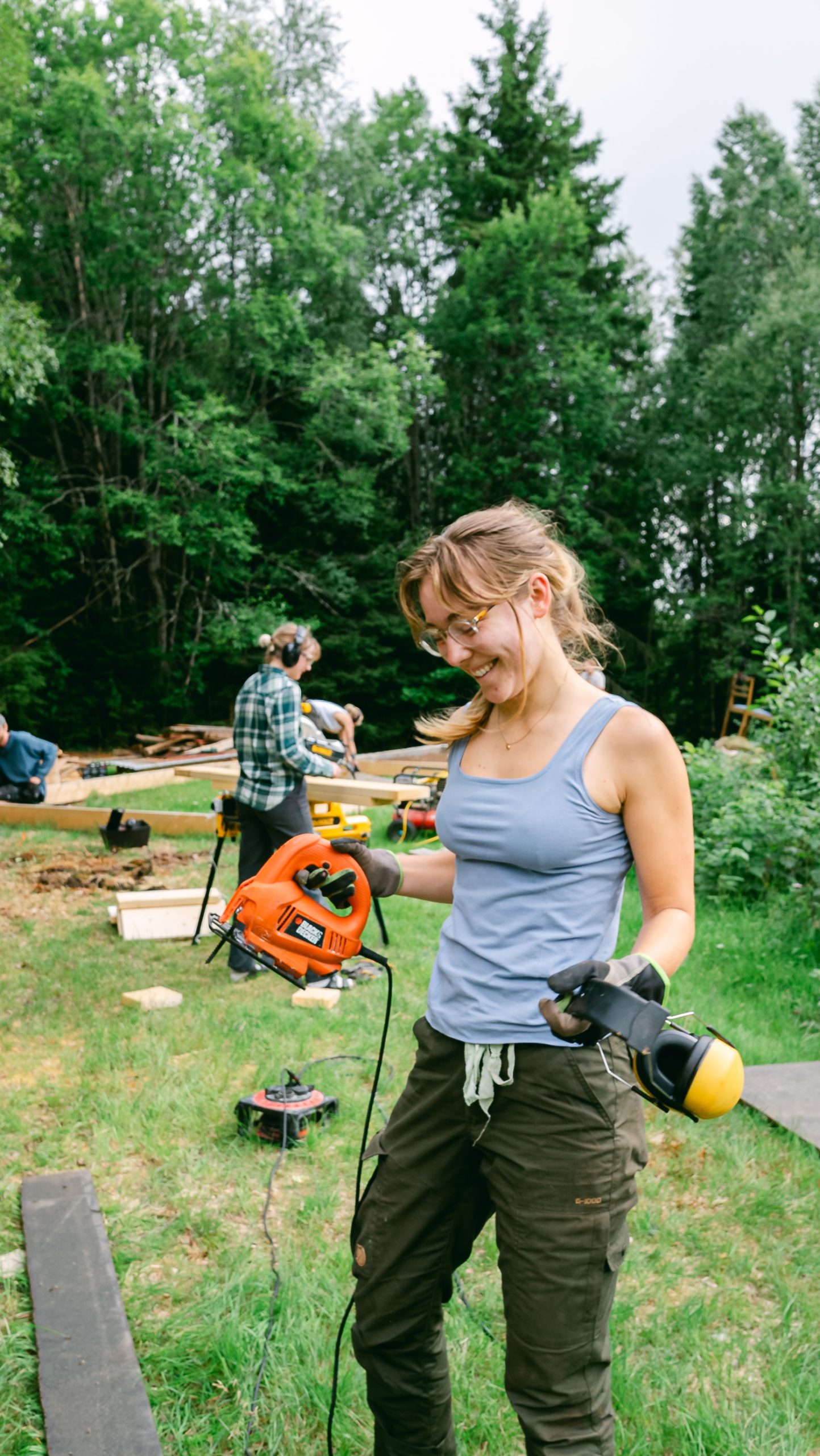 A happy volunteer holding power tools and ear protections while looking at their project.