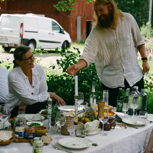 Swedish man and women by the midsummer food at the dinner table in the garden.