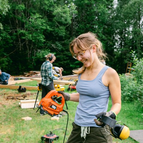 A happy volunteer holding power tools and ear protections while looking at their project.