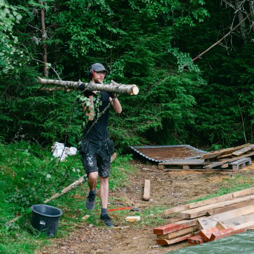 A volunteer carrying a big log from the forest to the tiny house project.